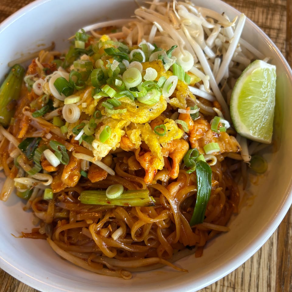 A close-up of Thai Taste's Pad Thai, garnished with bean sprouts, green onions, and a lime wedge.
