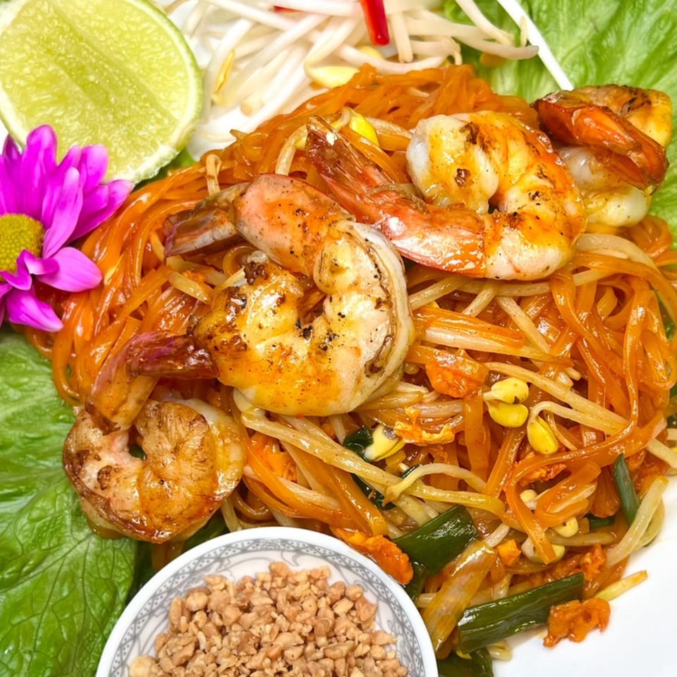 Thai Taste's shrimp Pad Thai with lime, bean sprouts, peanuts, and a purple flower garnish.