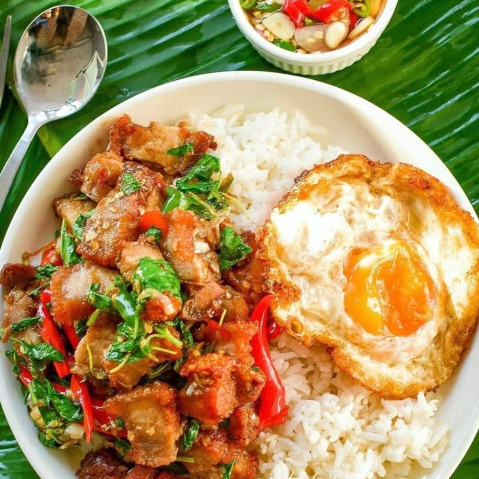 Thai Taste's crispy pork belly with basil, rice, and a fried egg, served on a banana leaf.