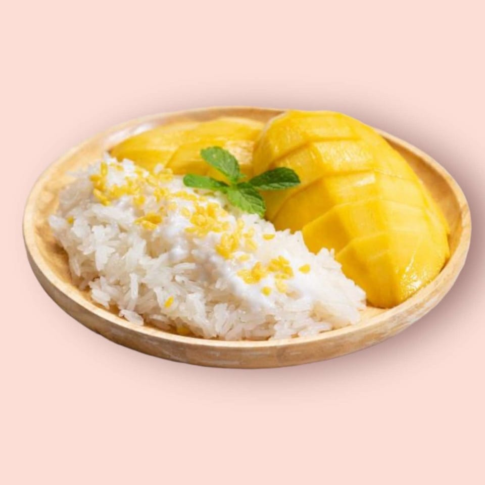 Mango sticky rice with coconut milk and a mint garnish on a wooden plate.